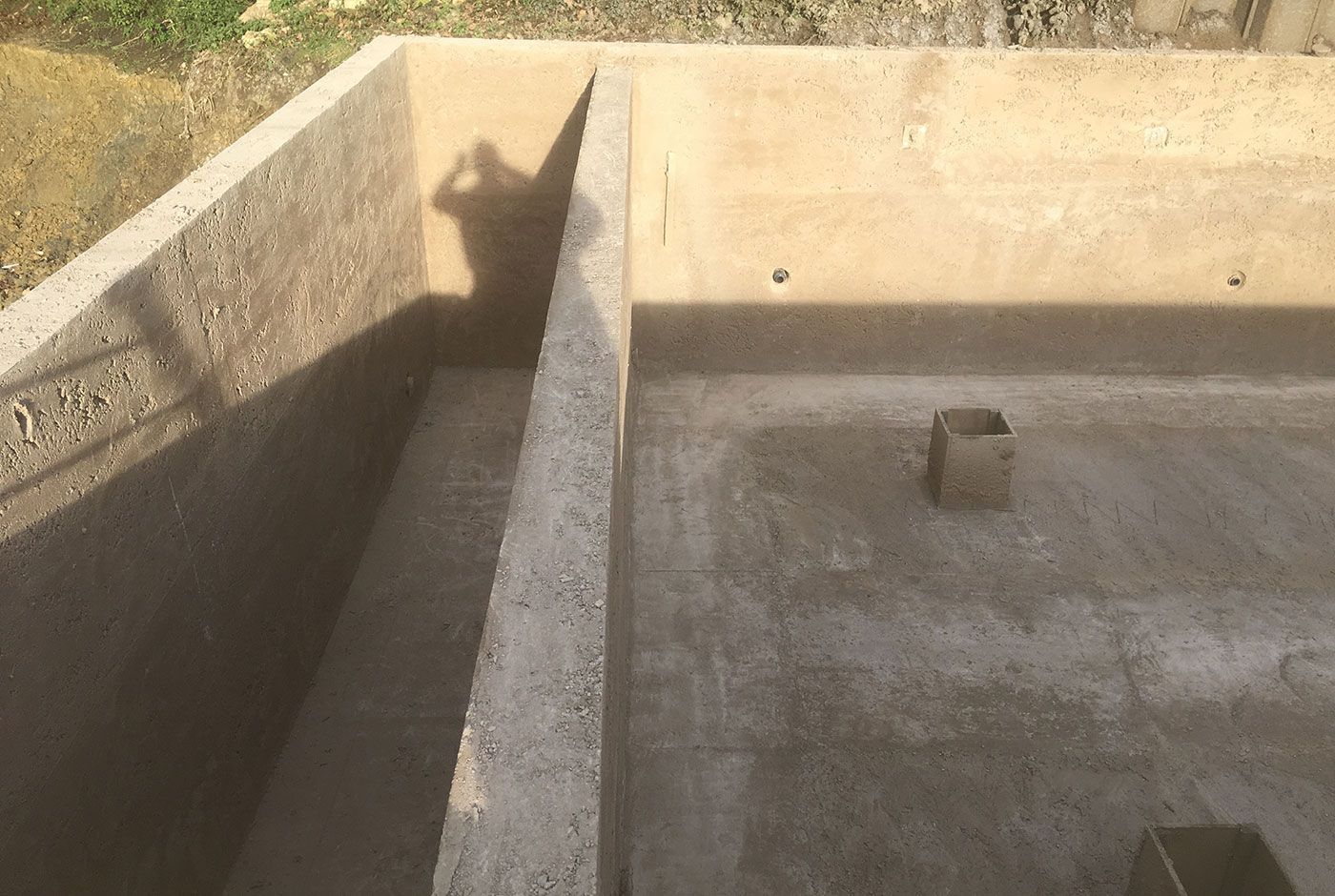Concrete shell of an infinity pool, with a person’s shadow on the wall.