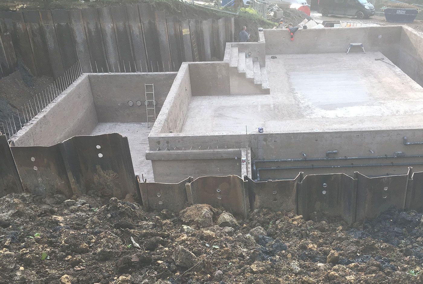 Concrete foundation of an infinity pool  with poured slab and retaining walls in a muddy excavation area.