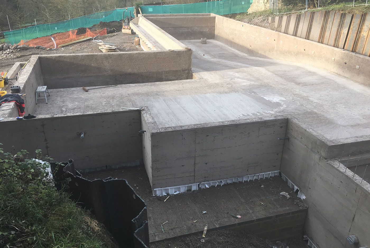 The concrete shell of an infinity pool under construction, with large retaining walls, ramps, and a dirt path