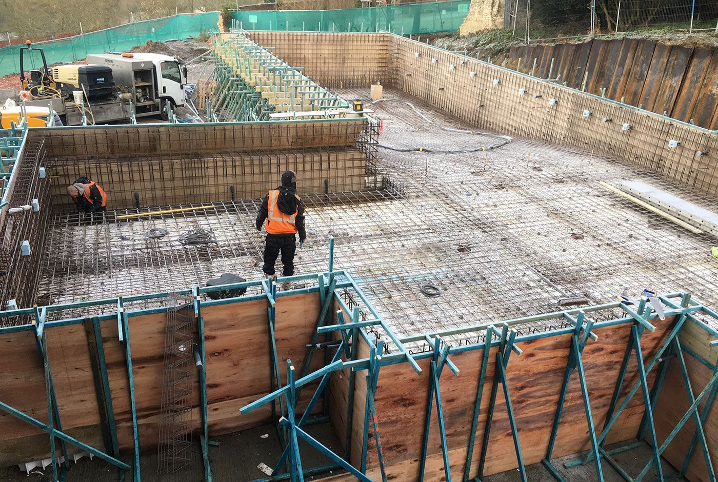 Construction workers on the site of an infinity pool foundation pit with rebar and wooden formwork.