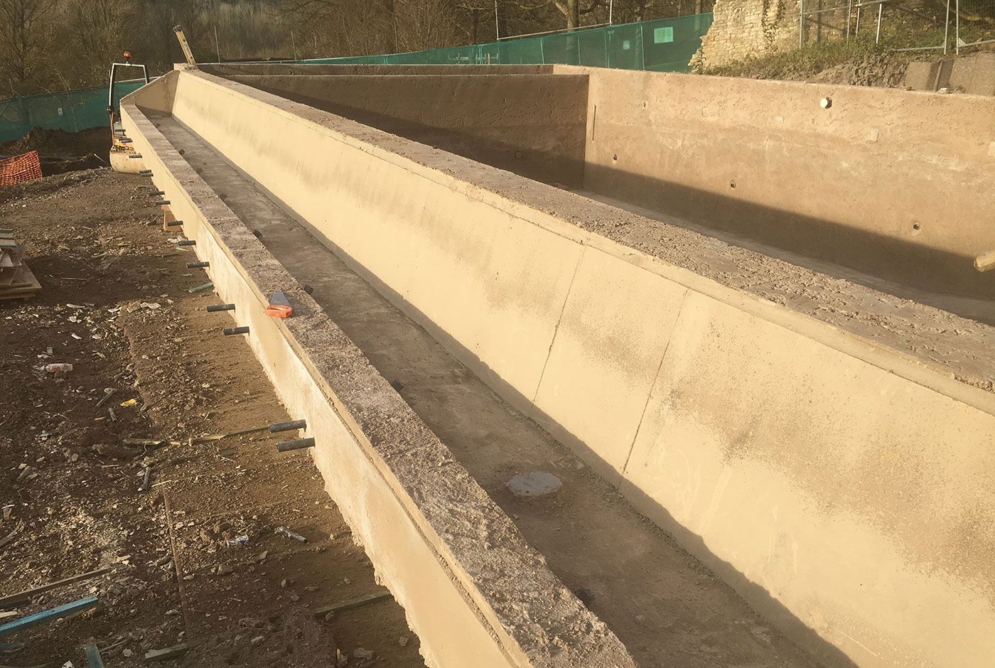Concrete shell structure  under construction with green fencing in the background.
