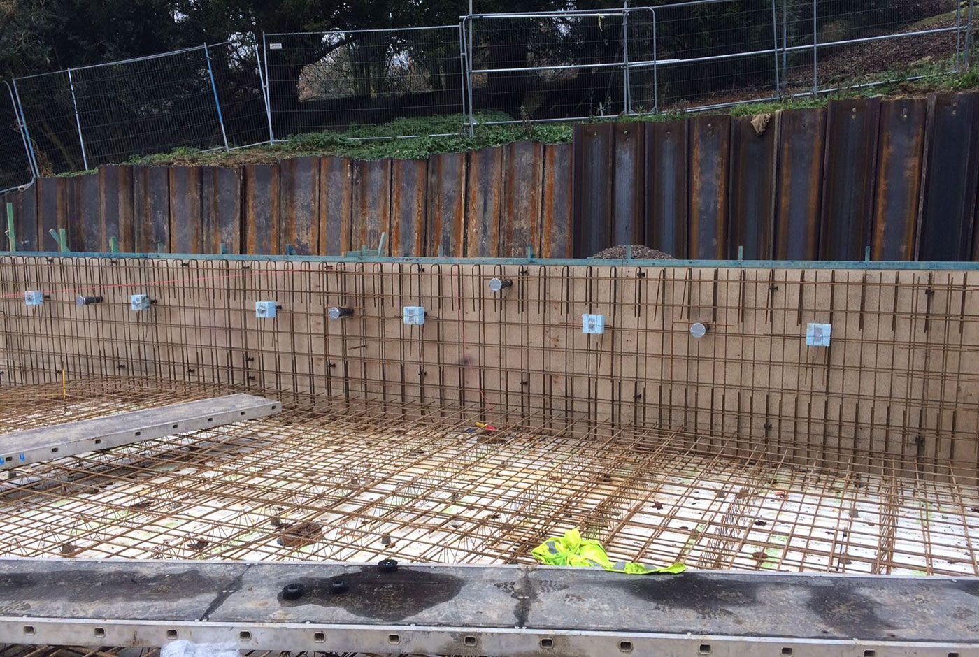 Swimming pool under construction against a steel-reinforced slope.