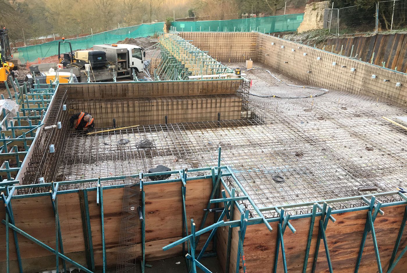 Construction workers on the site of an infinity pool foundation pit with rebar and wooden formwork.