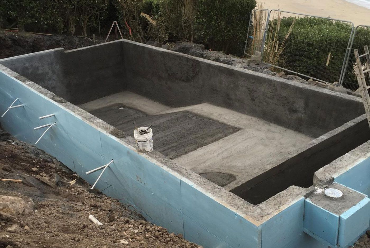 Empty concrete shell of an infinity pool still under construction and surrounded by dirt.
