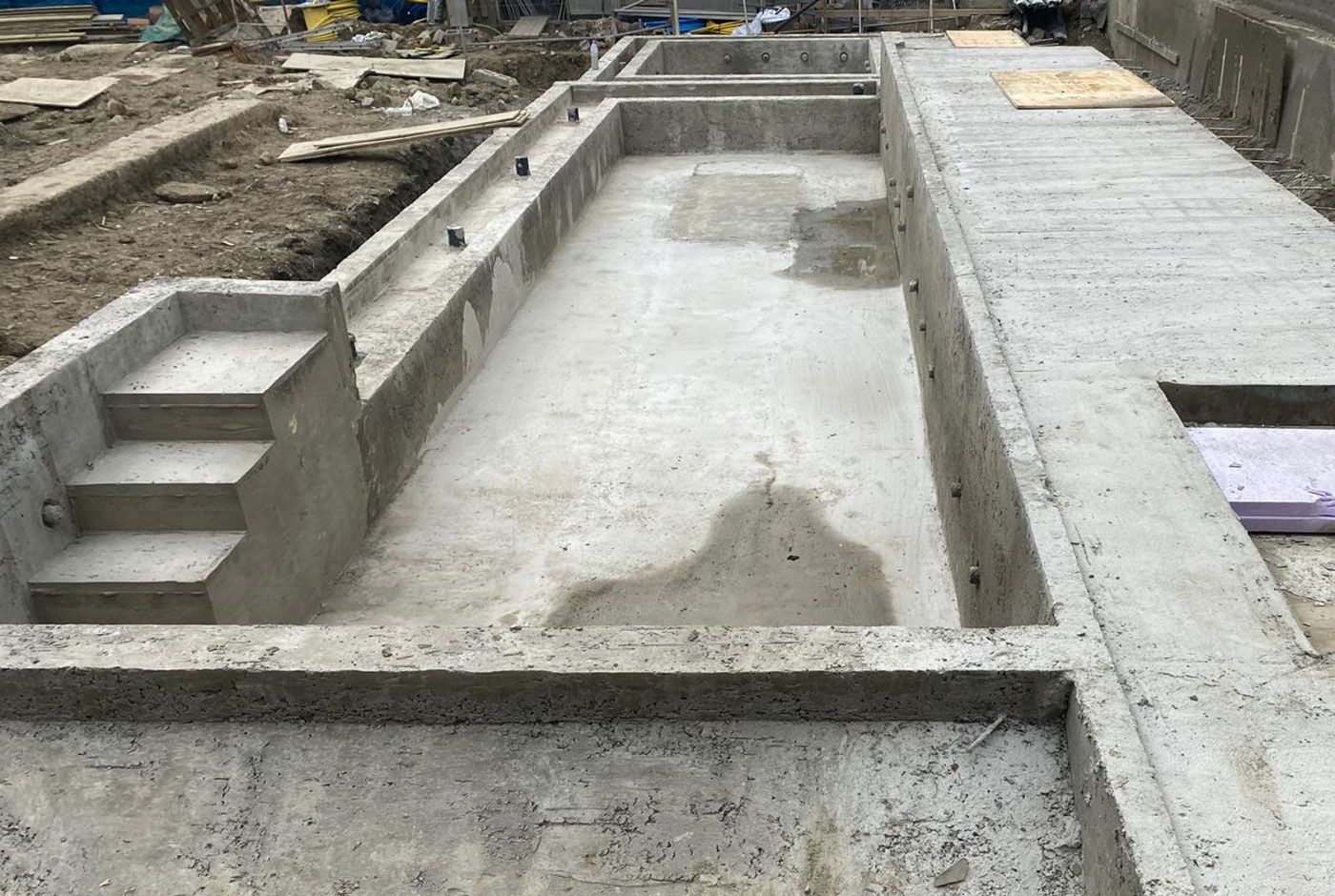 Infinity pool concrete shell under construction with a stepped section and surrounded by dirt and construction materials.
