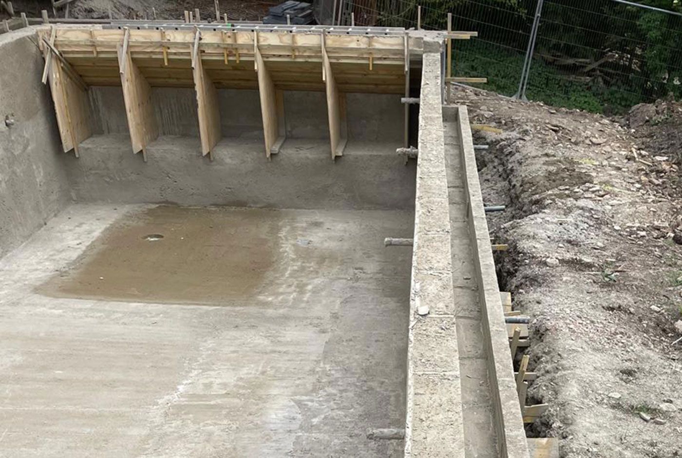 A section of an infinity pool shell made with concrete, with wooden formwork, rough ground surrounding it.