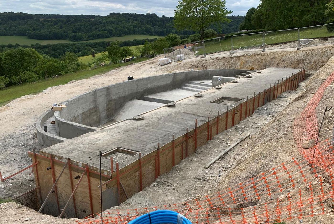 Concrete foundation excavation on a hillside, with rebar forms and a wooded landscape in the background.