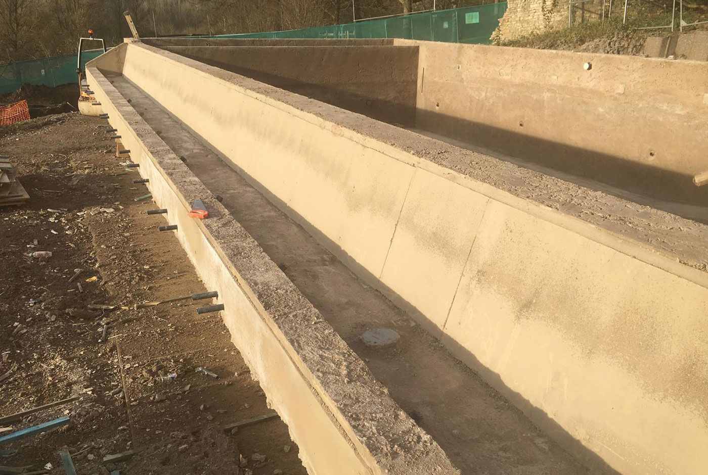 Detail of a concrete swimming pool shell under construction, lit by sunlight.