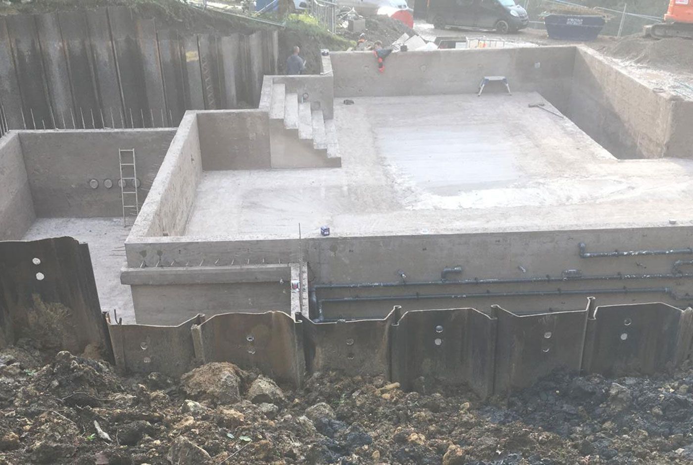 Concrete foundation of an infinity pool  with poured slab and retaining walls in a muddy excavation area.