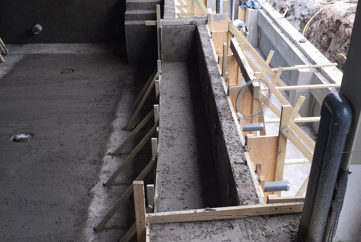 Construction in progress of an infinity pool shell with fresh concrete walls and base, and wooden formwork.