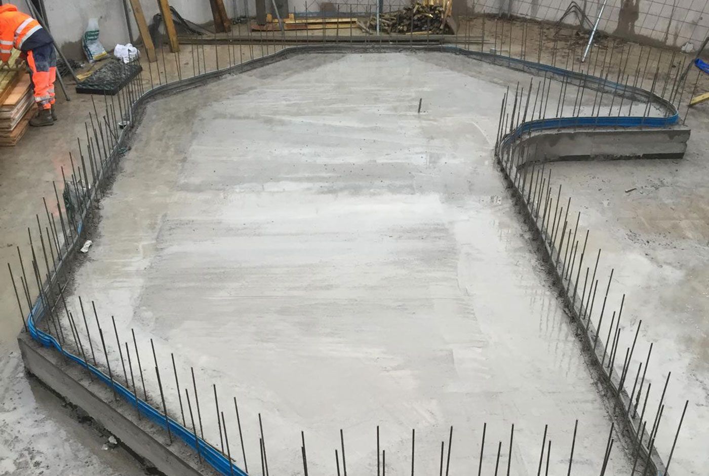 Freshly poured concrete slab foundation with exposed rebar in a construction site.