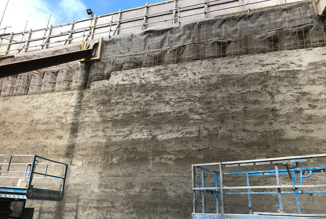 Concrete pile facing with scaffolding and safety railing on top.