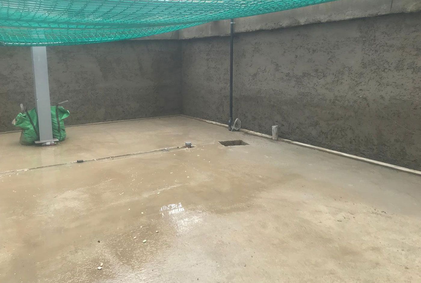 Walls and floor completed with spray concrete beneath green netting, floor is wet.
