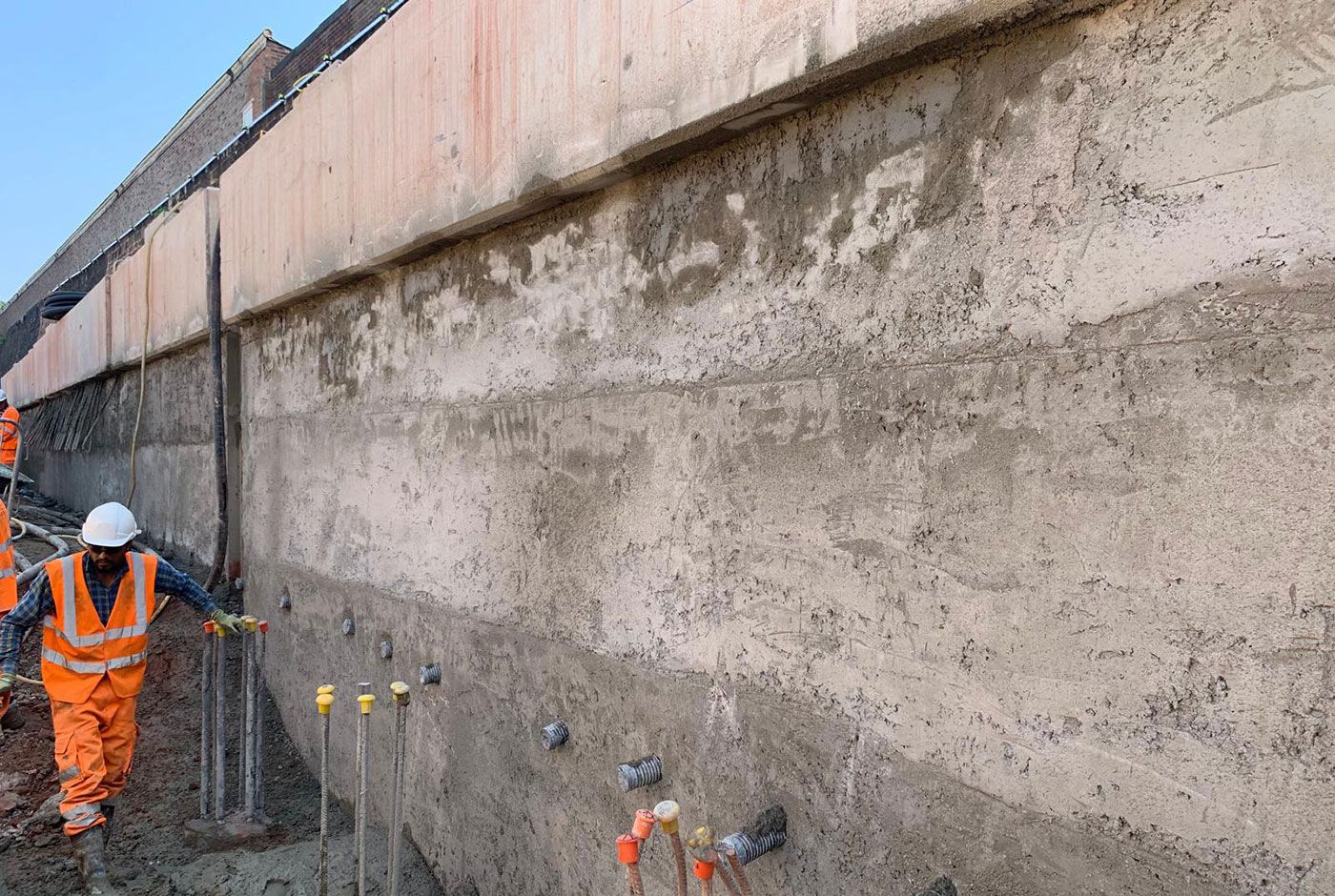 Workers in orange safety gear inspecting a concrete retaining wall at a construction site.