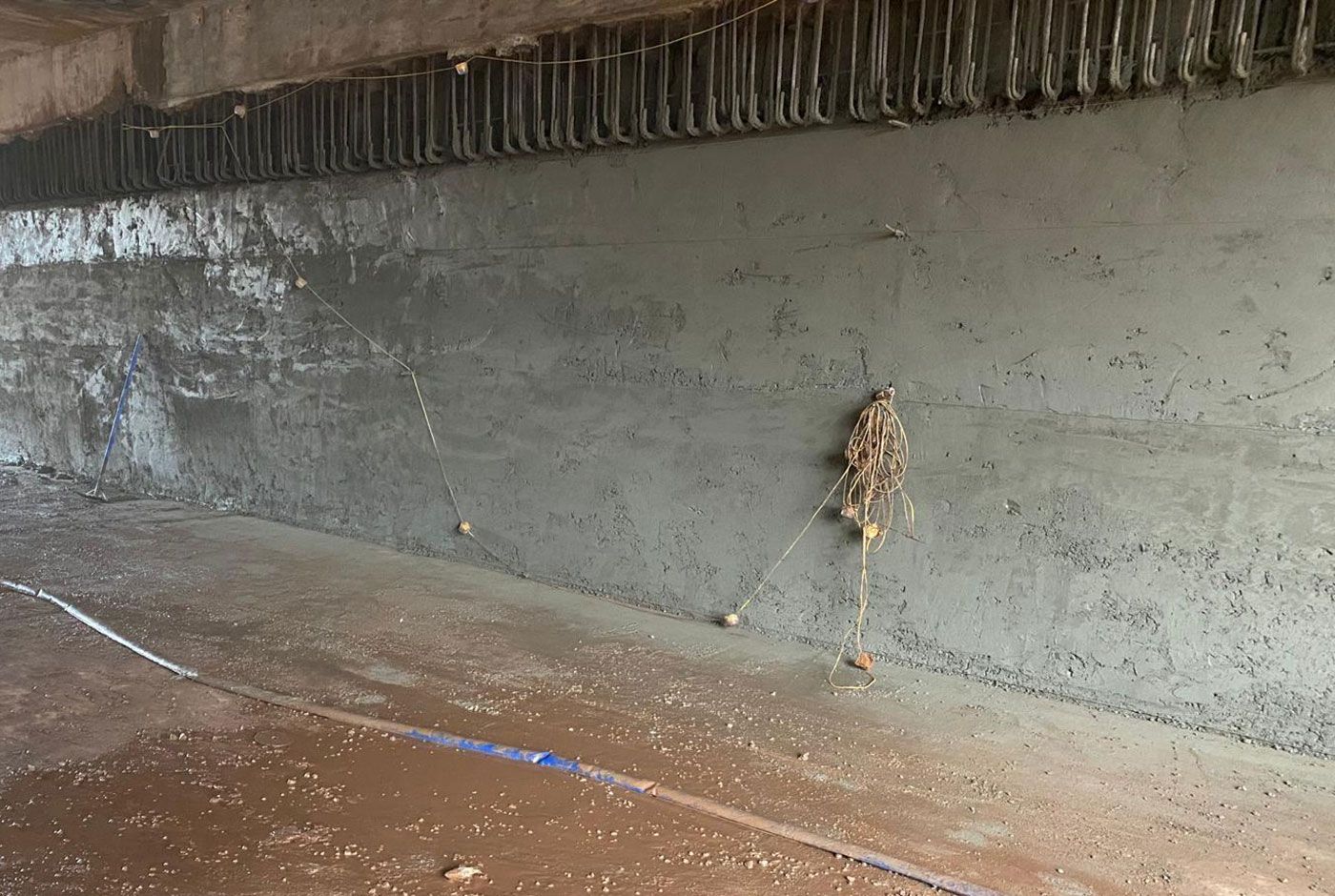 A roughly finished concrete wall with a wet, muddy floor and a trailing hose.