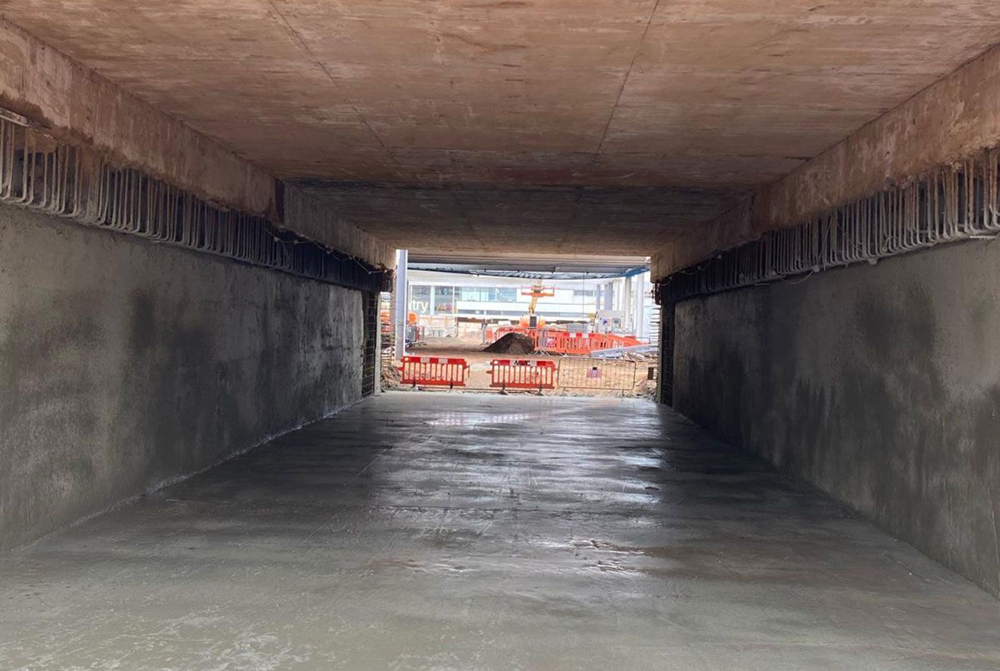 Empty concrete tunnel opening to a construction area with orange barriers in the distance, concrete is freshly applied.