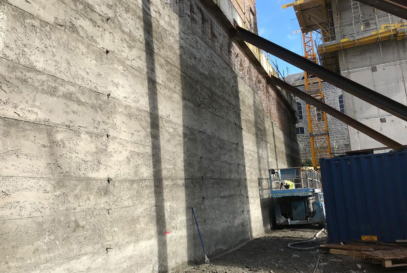 Construction site with a concrete wall, blue container, and scissor lift in the background.
