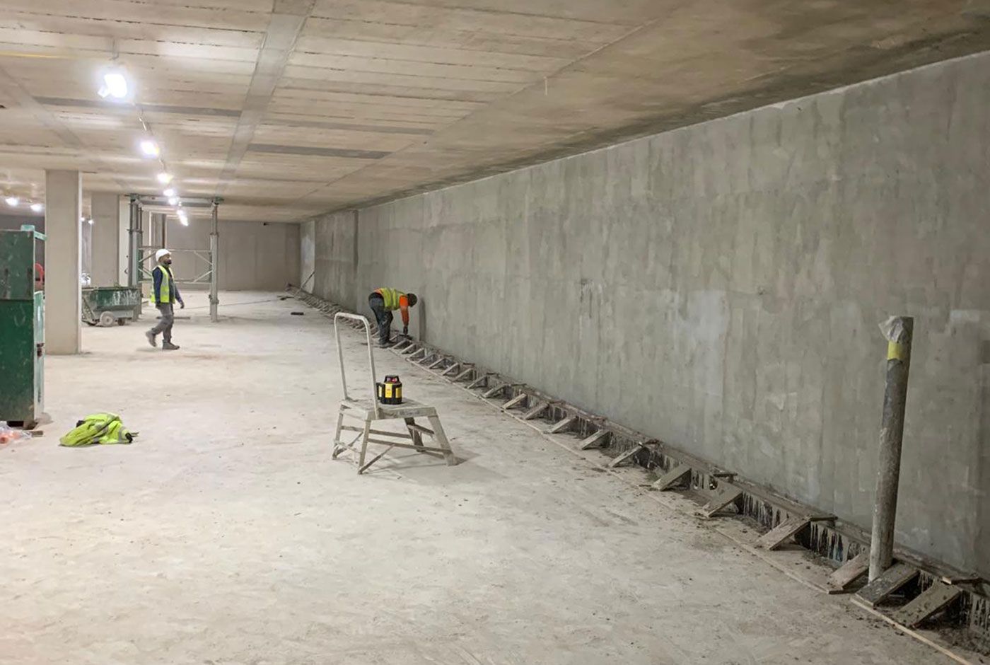 Construction workers in the interior of a concrete structure, lit by ceiling lights.