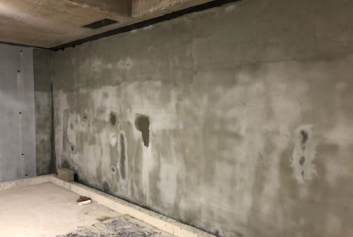 Unfinished concrete basement wall with dark water stains and a rough ceiling.