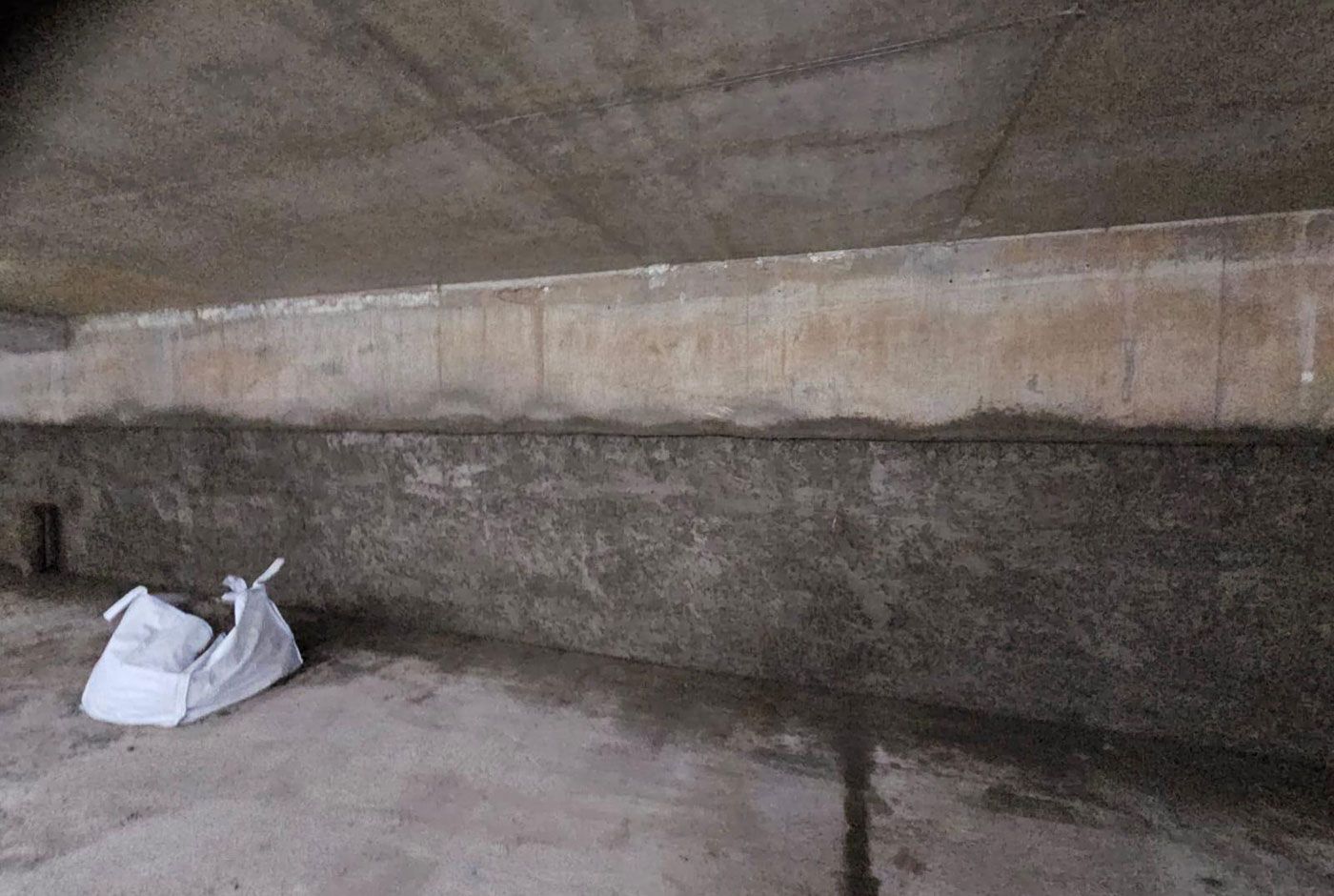A dimly lit interior space with concrete walls, floor and ceiling, a large white grab bag on the floor.