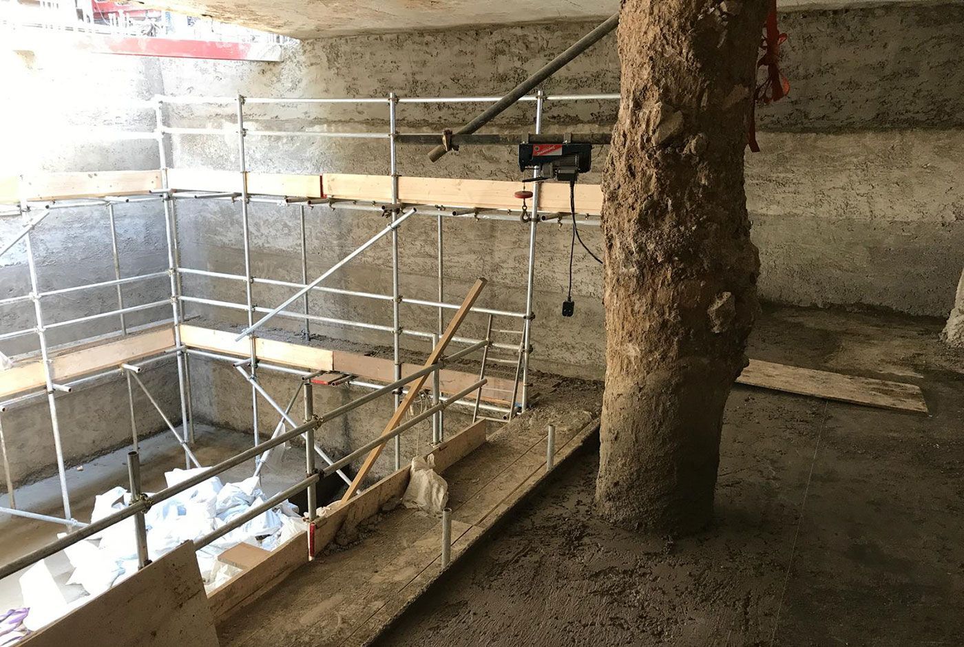 Construction site interior with scaffolding, large support column and walls and floors freshly concreted and unfinished.