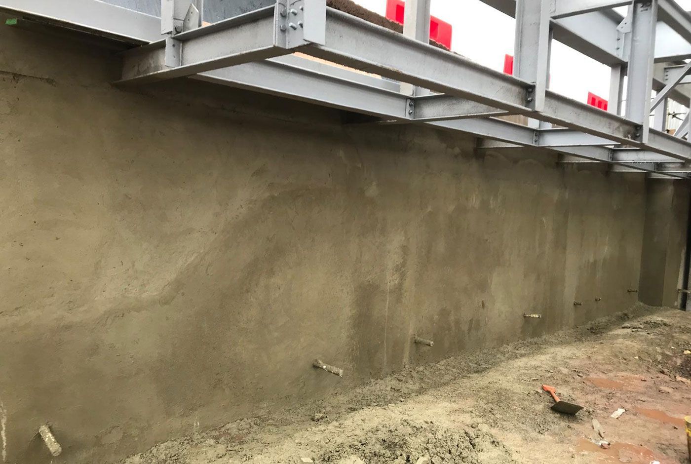 Sprayed concrete retaining wall beneath an elevated structure on a construction site.