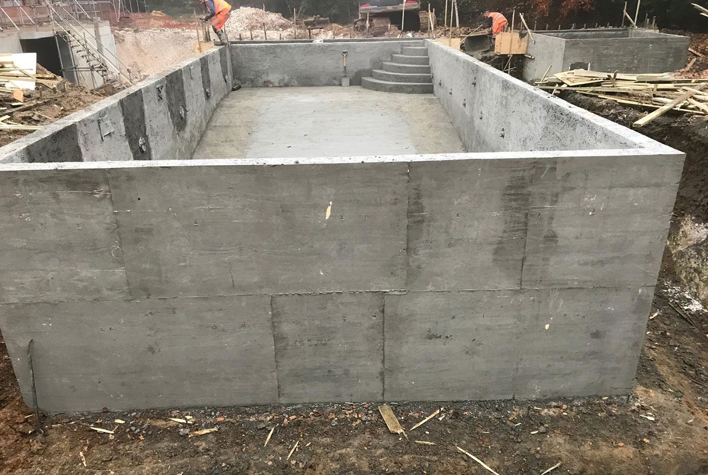 Rectangular concrete shell of an outdoor skimmer pool, surrounded by construction materials and debris.