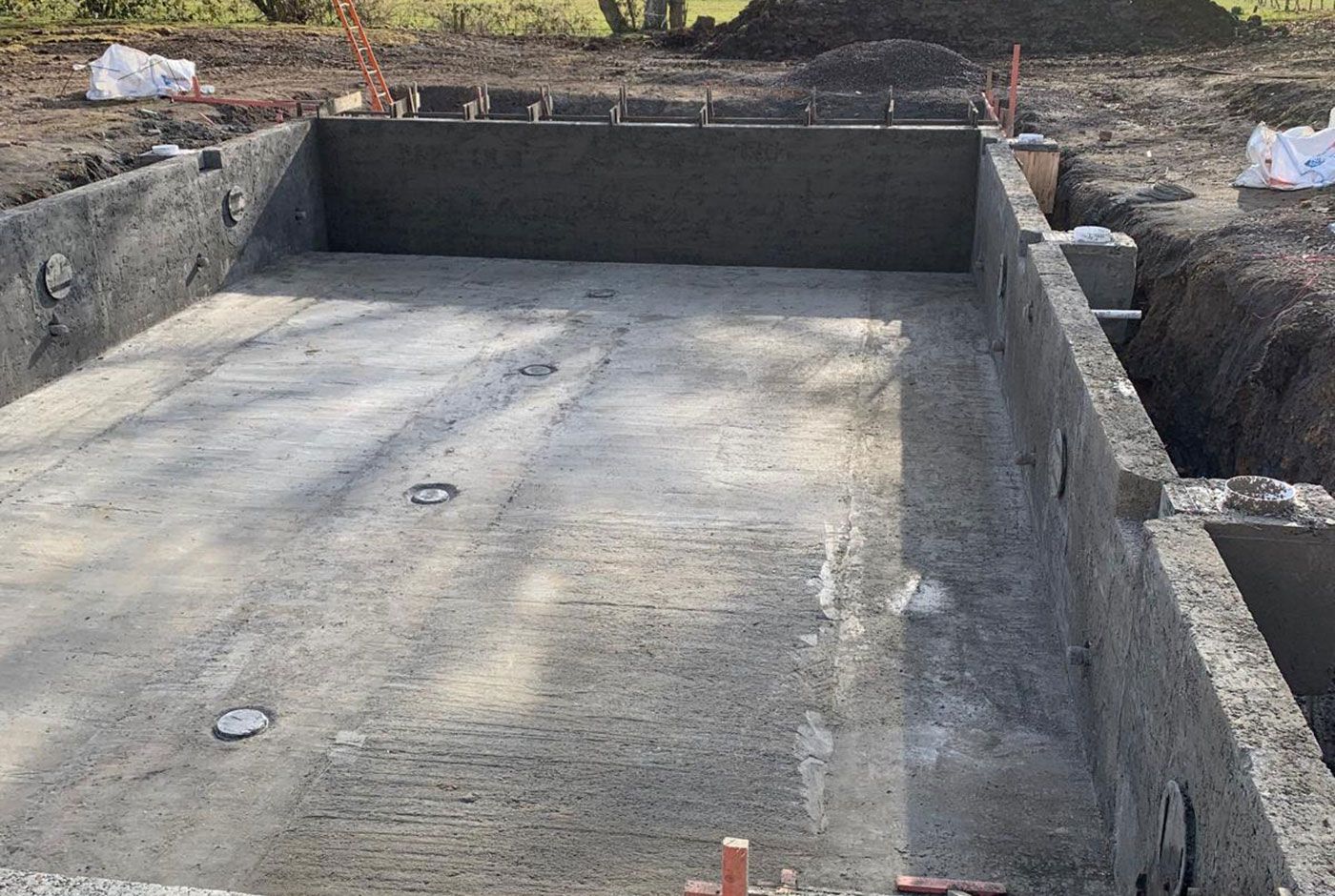 Concrete foundation footing at a construction site, with unfinished trench walls and soil around it.