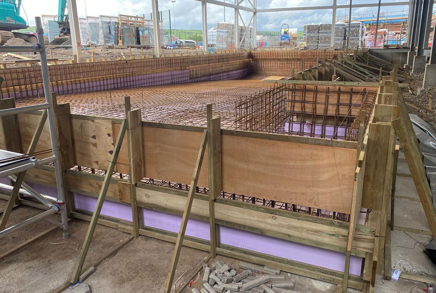 Early construction phase of a skimmer pool, with wooden formwork and rebar, part of a large development scheme.