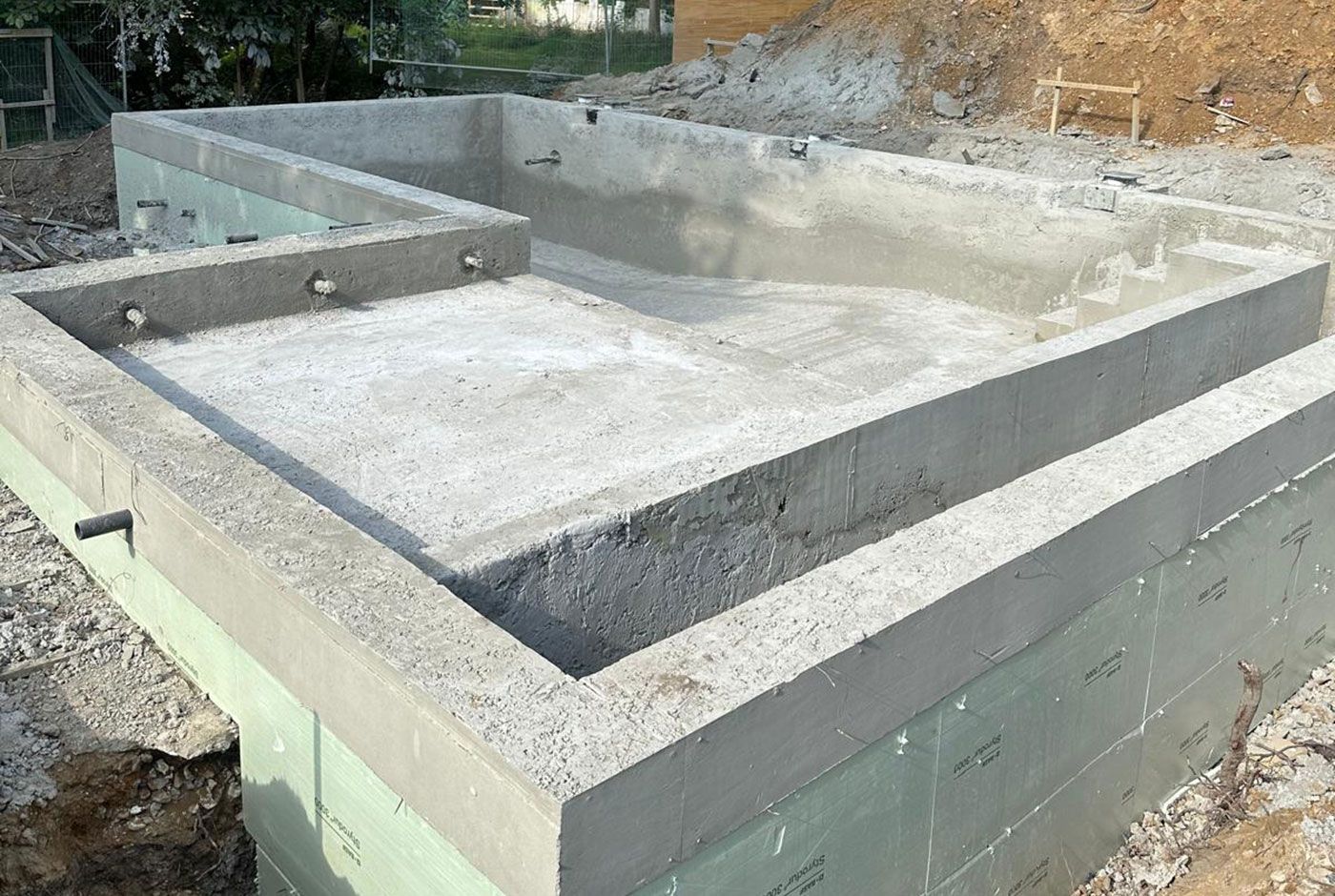 The concrete shell of an outdoor skimmer pool with excavated material in the background.