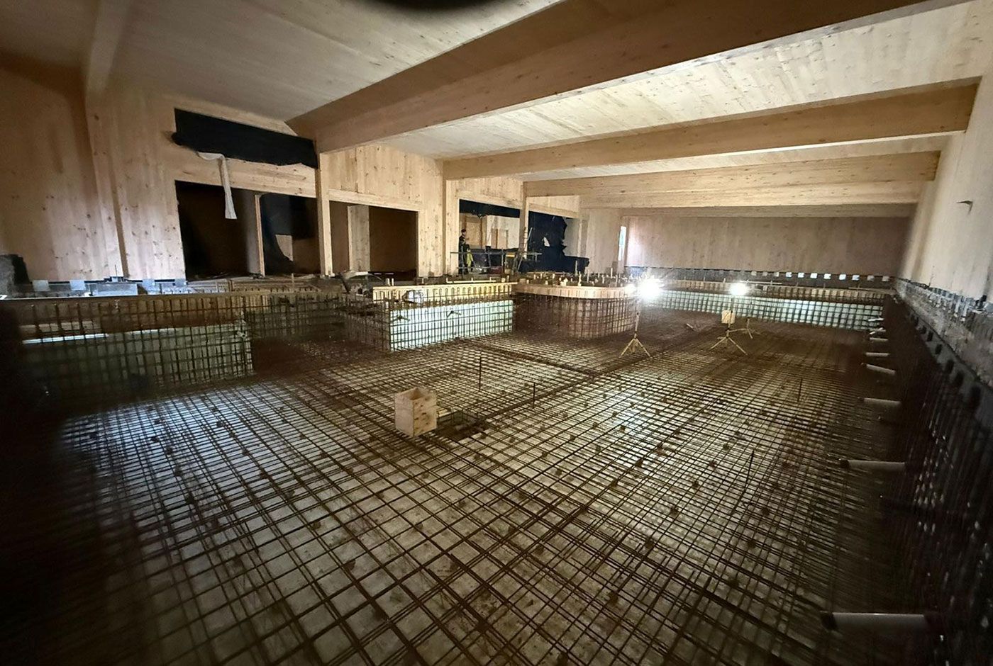 Indoor skimmer pool under construction with  metal mesh grid visible on the walls and base, under warm lights.