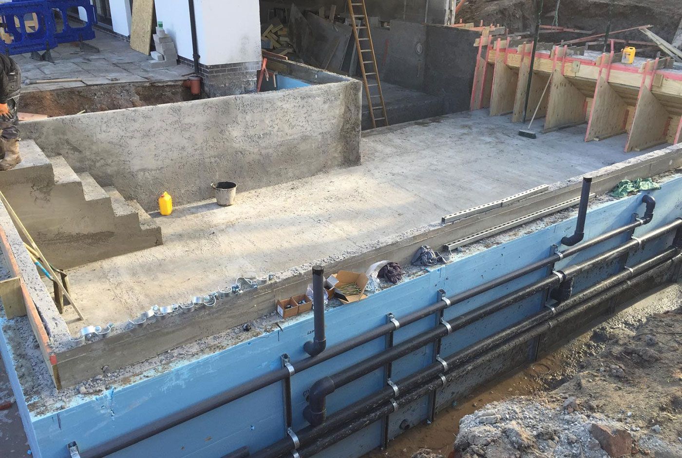 A concrete skimmer pool shell under construction with walls, rebar, base and steps, pipework visible in the foreground.