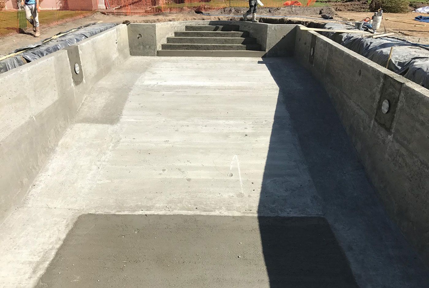 An outdoor skimmer pool under construction with steps at the far end and a sloping base.