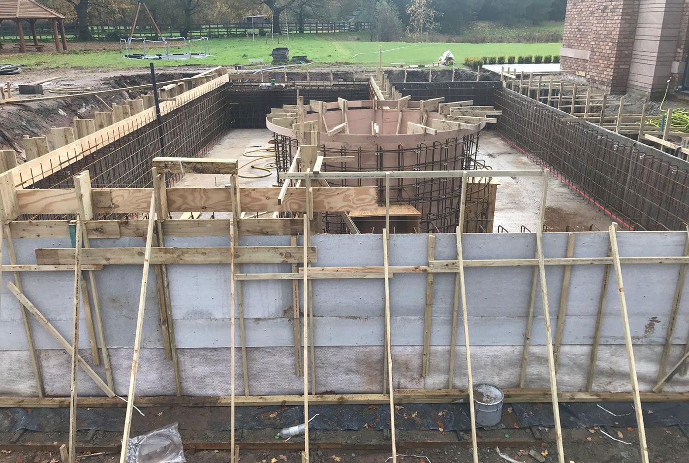 Construction site of an outdoor swimming pool with wooden formwork and concrete foundation walls in progress.