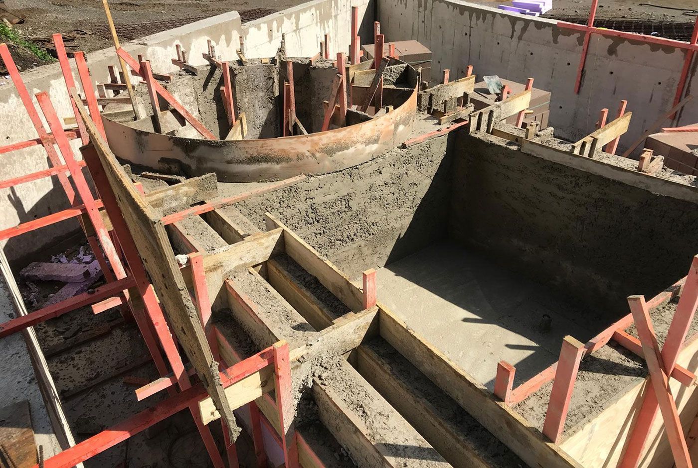 Rough concrete pool shell with circular spa feature under construction with wooden forms and red support struts.