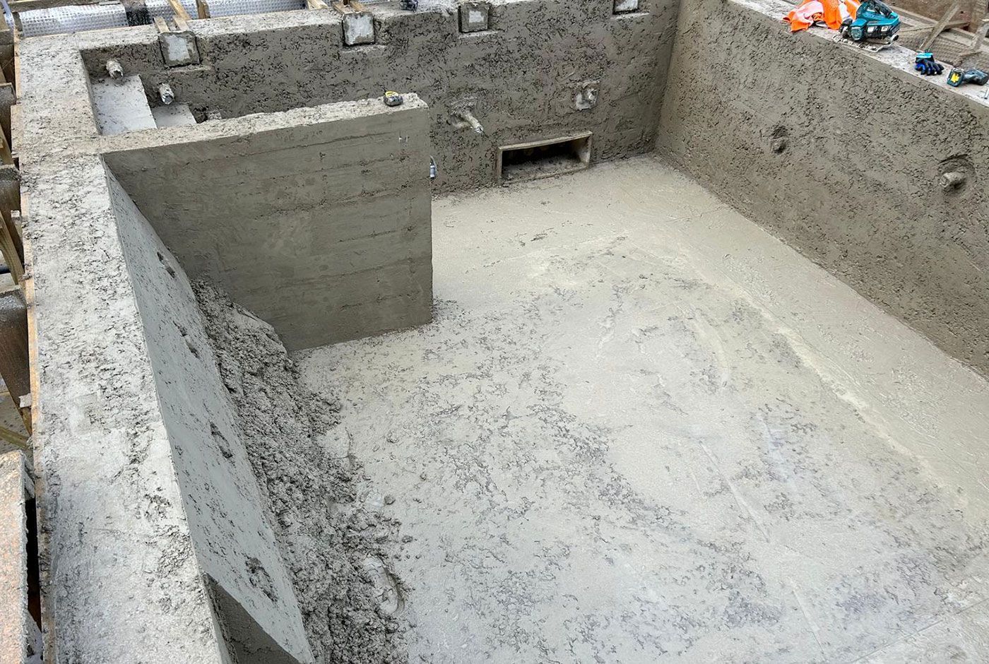Concrete shell of a rectangular spa pool under construction with a small partition wall and rough concrete surface.