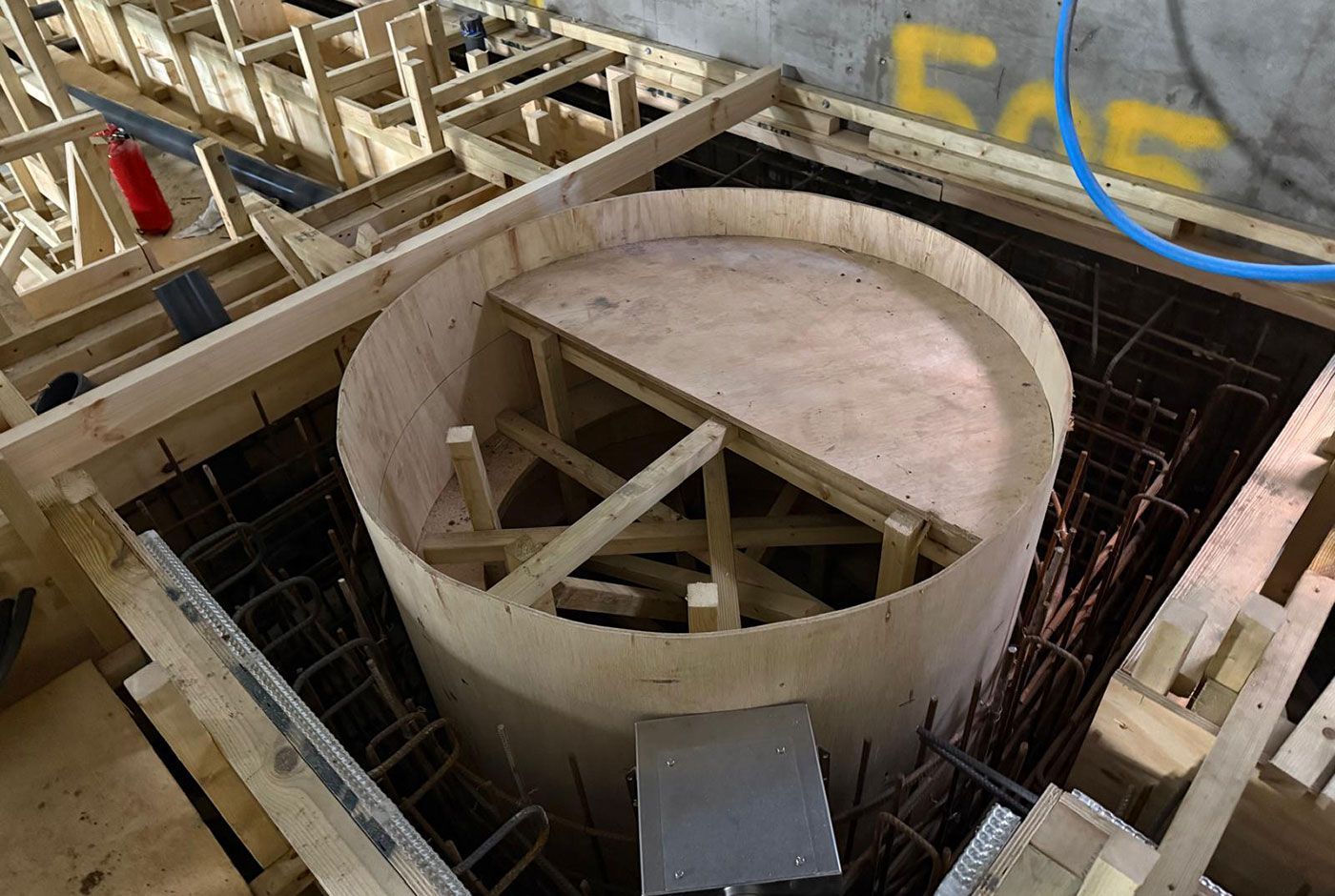 Circular pool structure under construction with wooden formwork and rebar within a larger building frame.