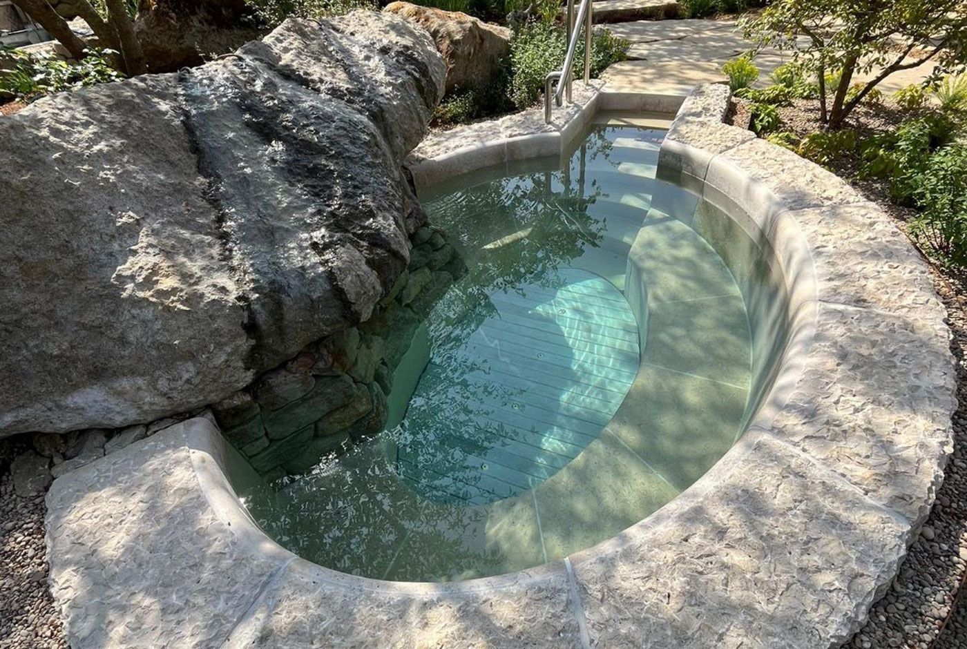 Outdoor stone plunge pool with clear turquoise water set among rocks and greenery.