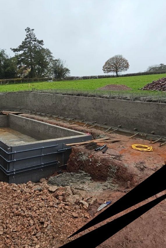 Rectangular swimming pool shell built on a hillside construction site, with a large  retaining wall to stabilise the slope.