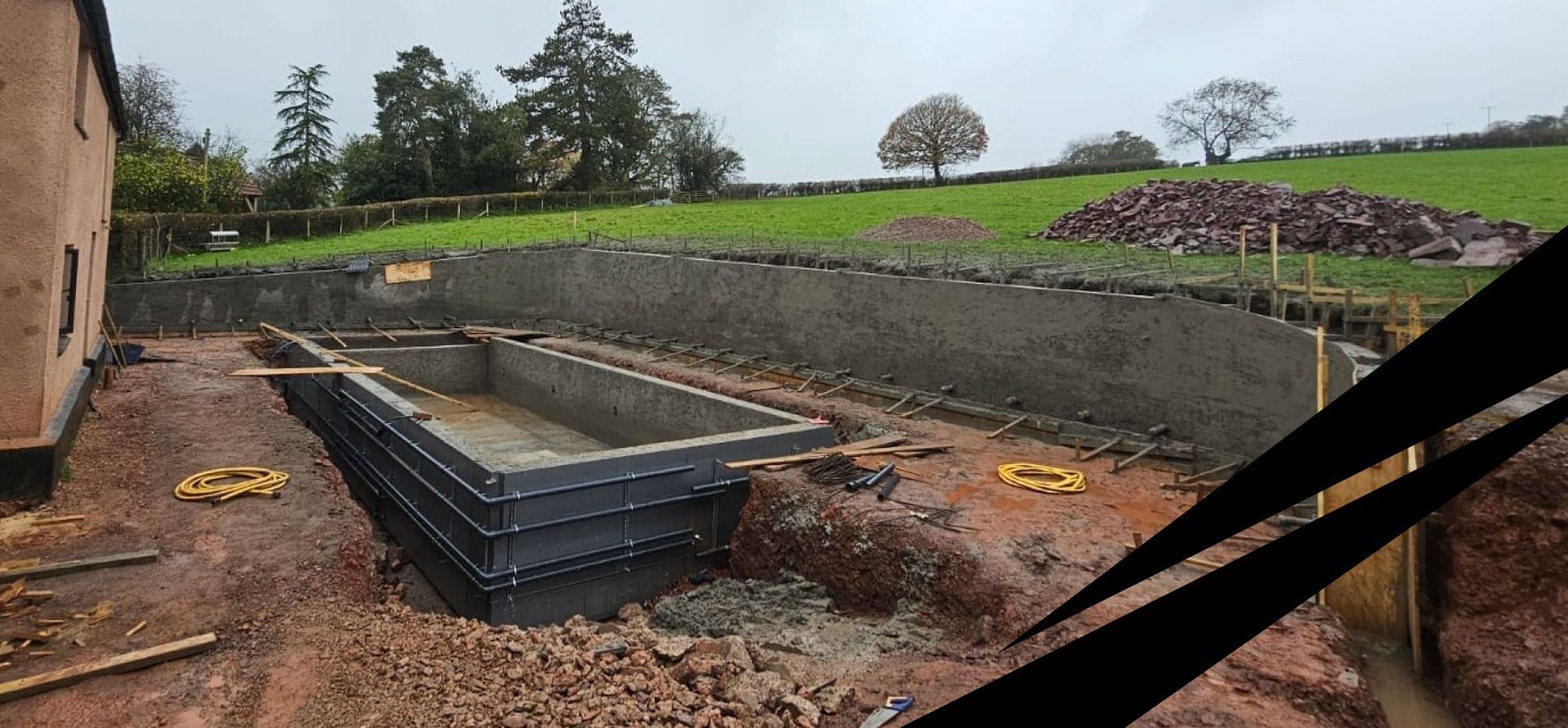 Rectangular swimming pool shell built on a hillside construction site, with a large  retaining wall to stabilise the slope.