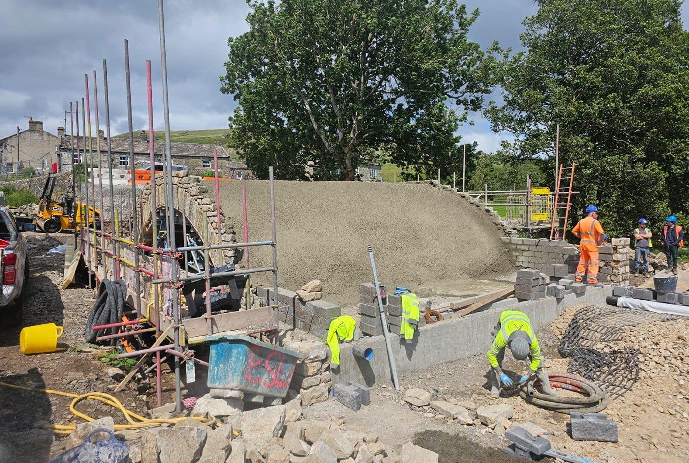 Workers at a construction site with scaffolding in a rural setting, fresh concrete applied to the top of a tunnel .