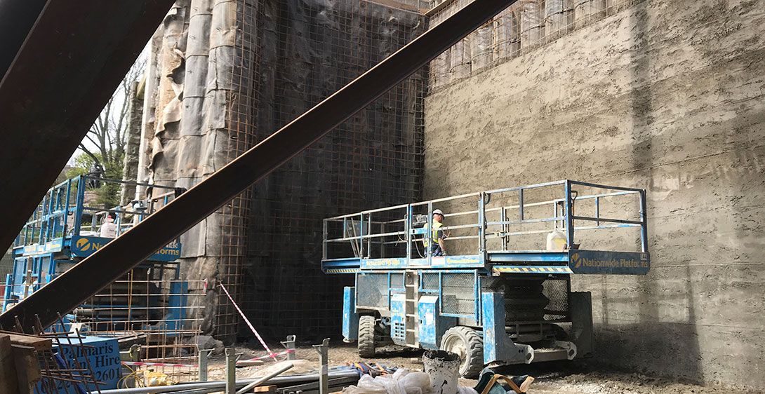 Blue scissor lift ready for use and parked next to contiguous piled walls.