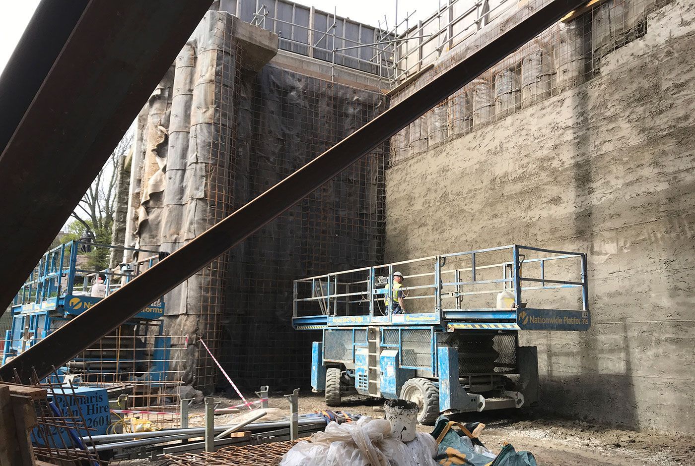 Blue scissor lift ready for use and parked next to contiguous piled walls.