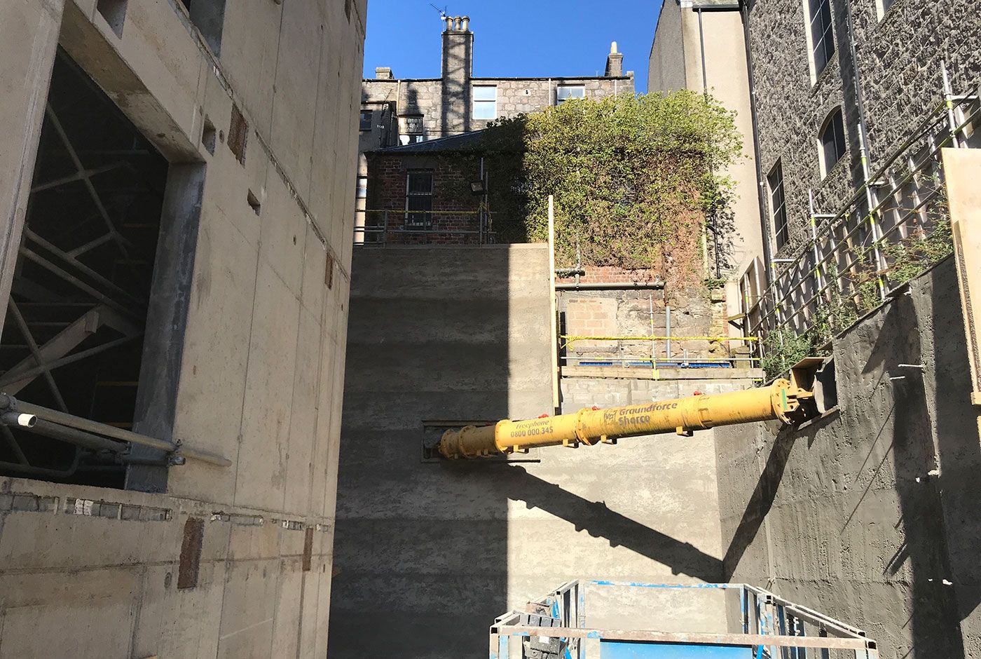 Urban construction site with concrete walls, a yellow pipe and scaffolding.