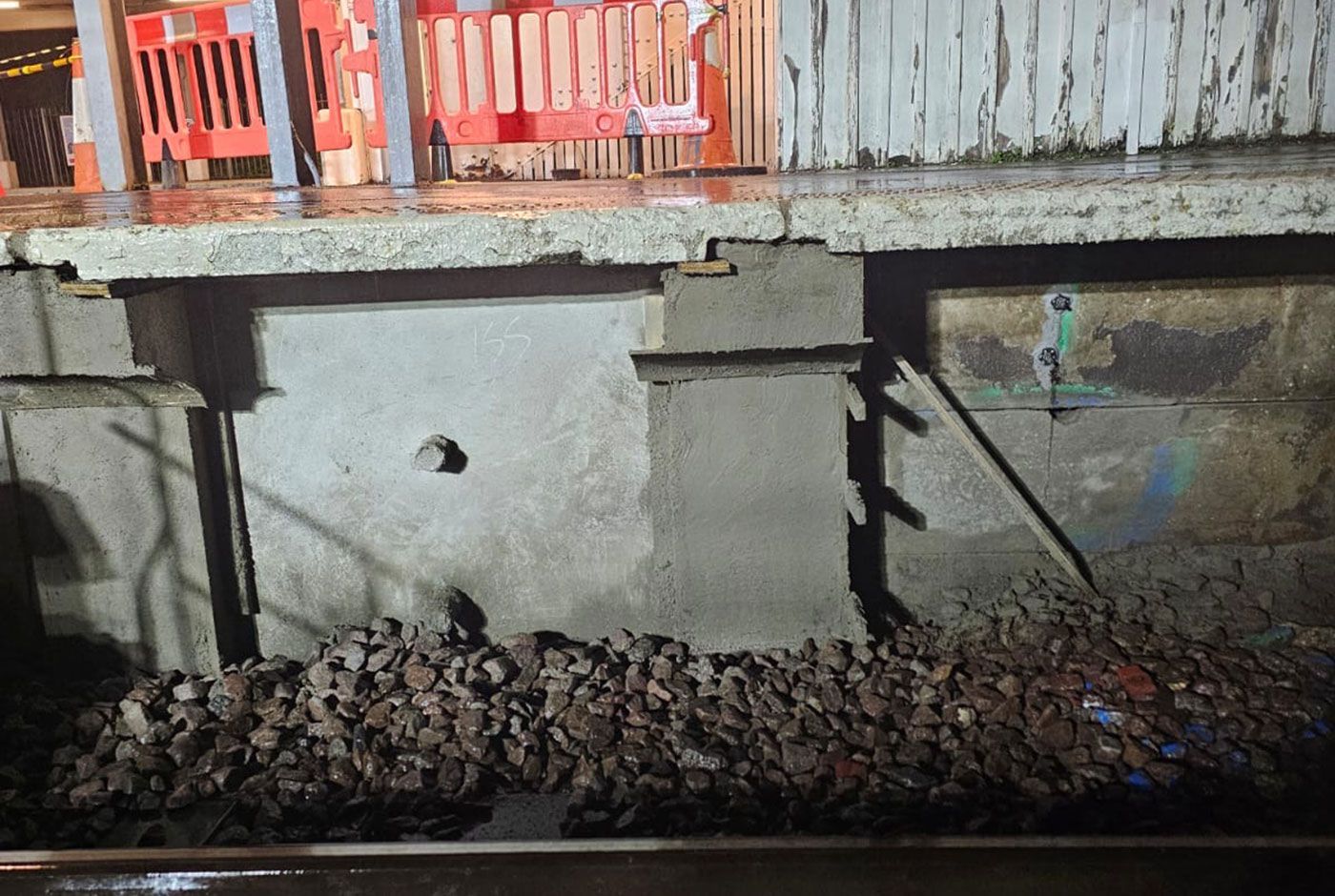Concrete wall of a railway platform under repair, with rocky gravel at the base.