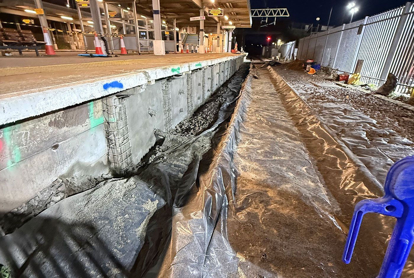 Railway platform at night, with platform wall to be repaired, rail tracks covered with tarpaulin.