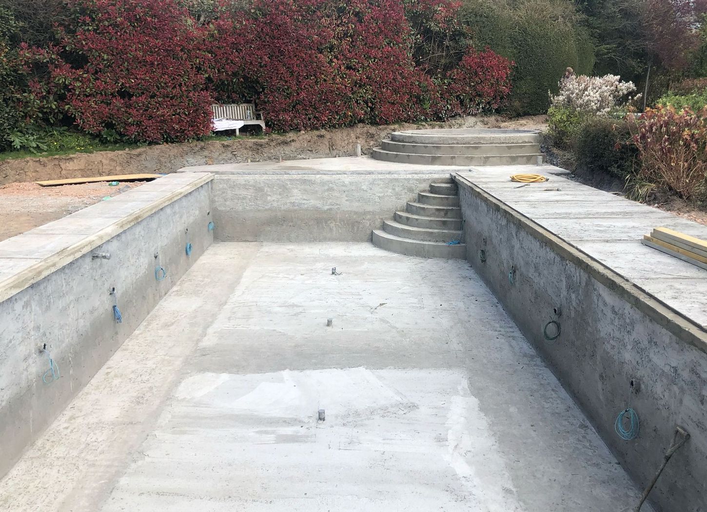 A newly constructed concrete swimming pool shell with integrated steps, set within residential grounds.