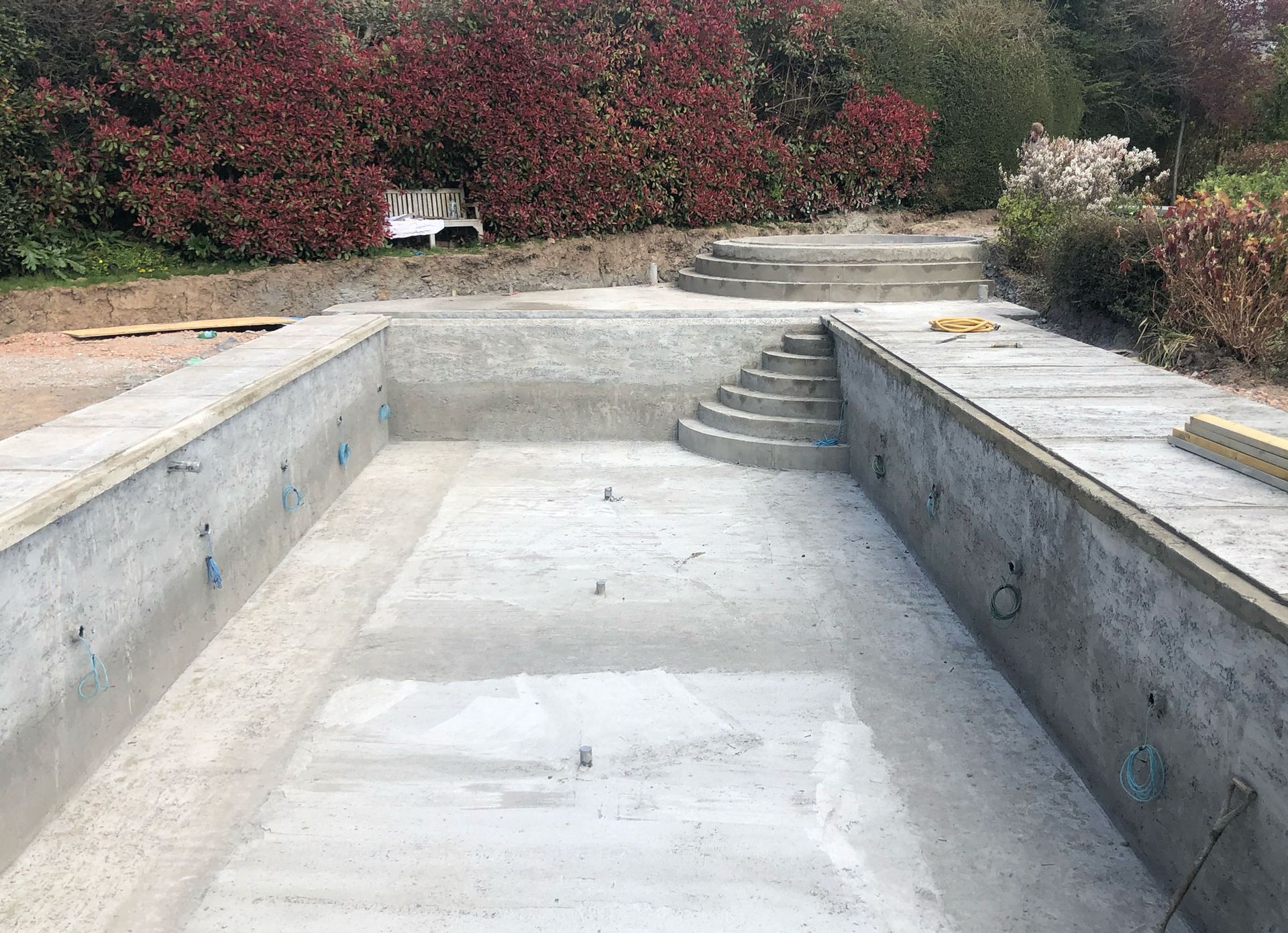 A newly constructed concrete swimming pool shell with integrated steps, set within residential grounds.