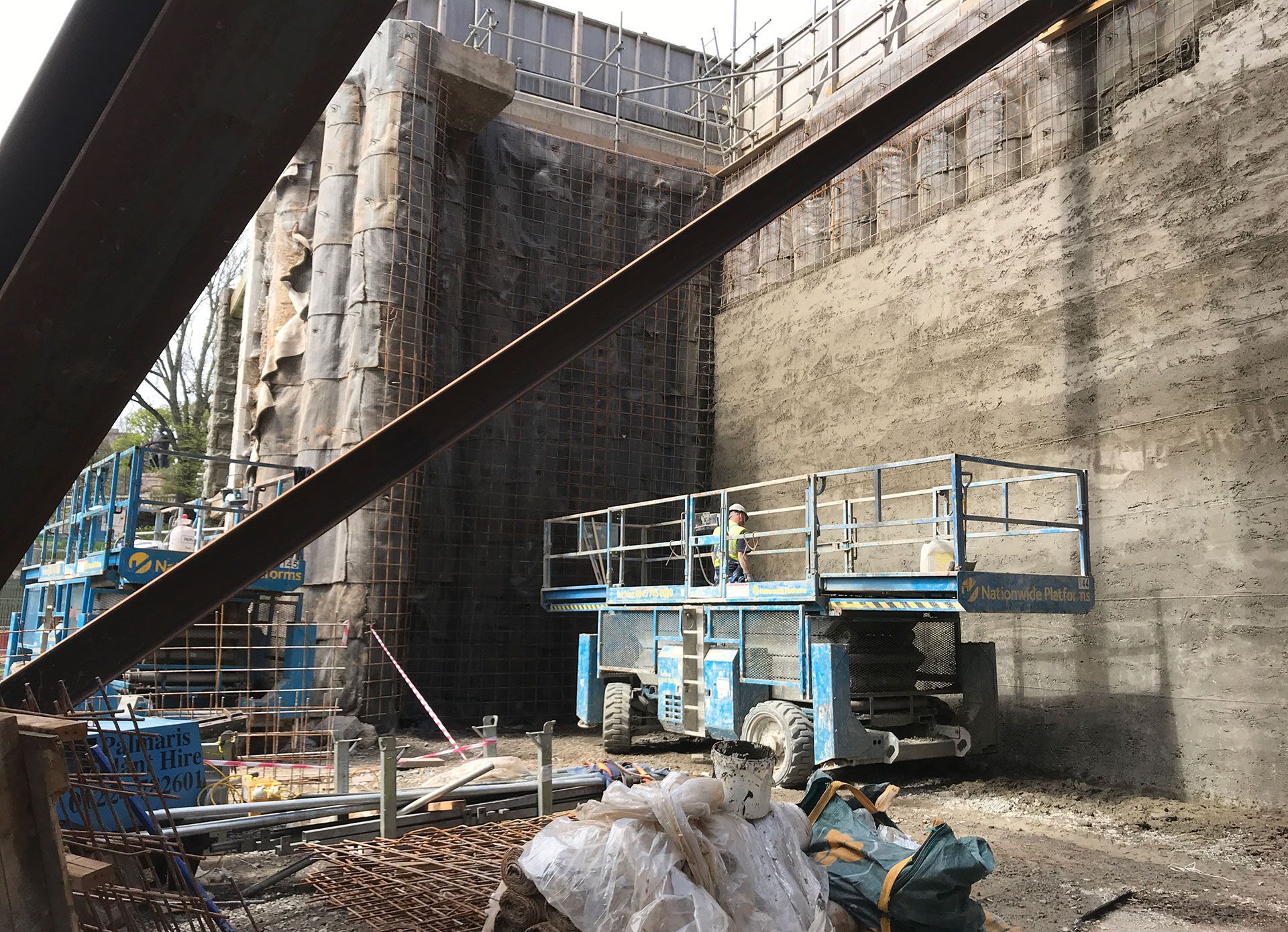 Blue scissors lift ready for use and parked next to contiguous piled walls.