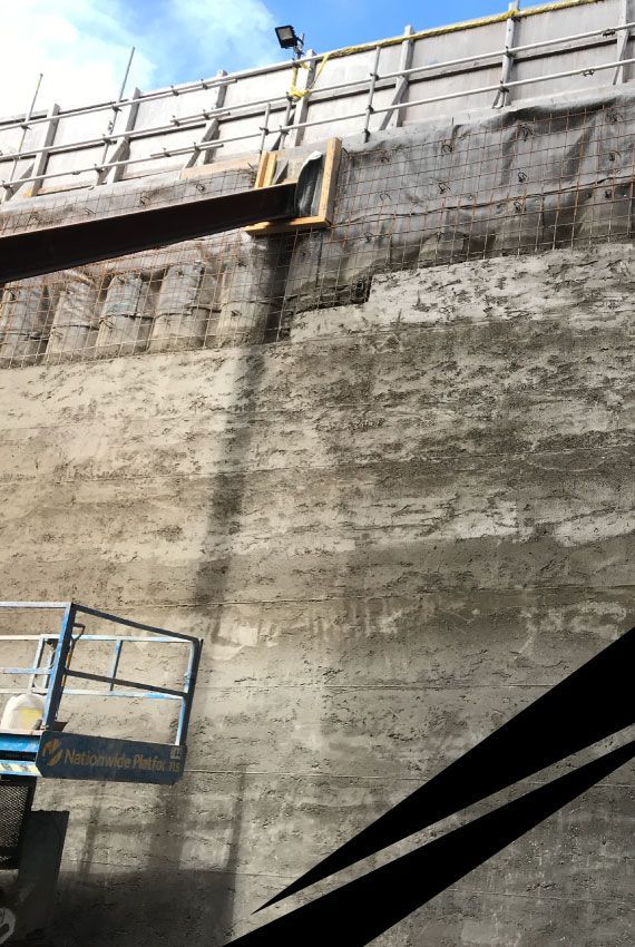 Contiguous wall with partly completed pile facing, barriers along the top and a bright sky above.